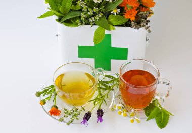 Bitkisel ilaç. Biberiye, nane, papatya, kekik, melissa, lavanta ve ilk yardım kutusunda calendula. İki cam bardak infüzyon ön planda.