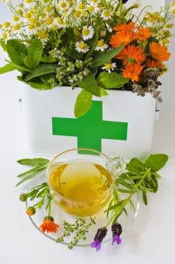 Alternatif Tıp. Biberiye, nane, papatya, kekik, melissa, lavanta ve ilk yardım kutusunda calendula. Cam bardak ön planda bitkisel infüzyon.