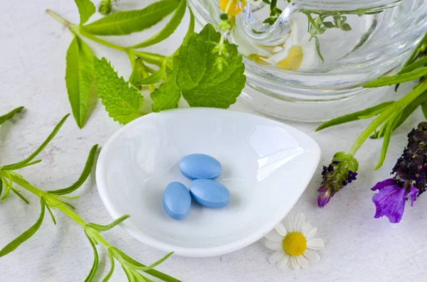 Alternative Medicine. Herbal Therapy. Blue pills and fresh healing herbs. White background.