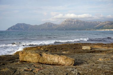 Taş plaj, deniz dalgaları ve dağ manzarası üzerinde arka planda günbatımı zamanı. Mallorca Adası, İspanya, yaz 2018 güneyinde çekilen bu manzara.