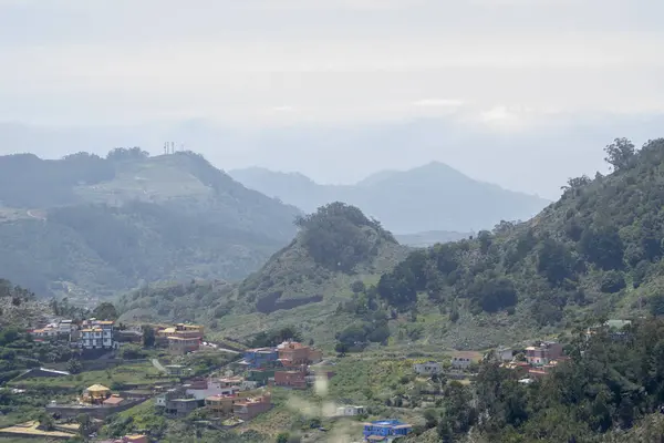 Dağın tepesinden Panarama. Dağlar, bulutlar, vadide bir köy, bir dağ yolu, dağ çiçekleri, ufukta okyanus