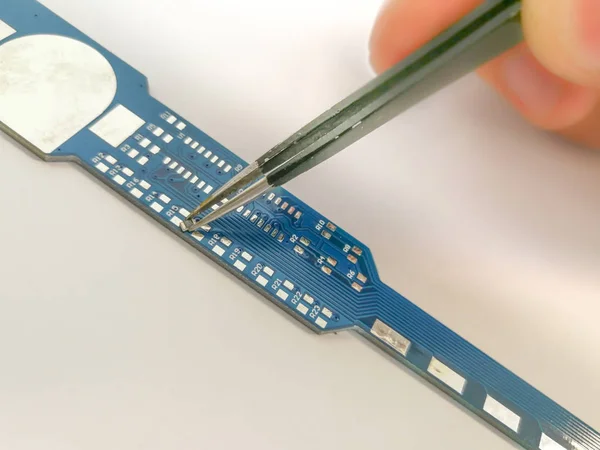Manual PCB assembly process by hand. Male hand holding tweezers with 0805 size Surface Mount Technology (SMT) component