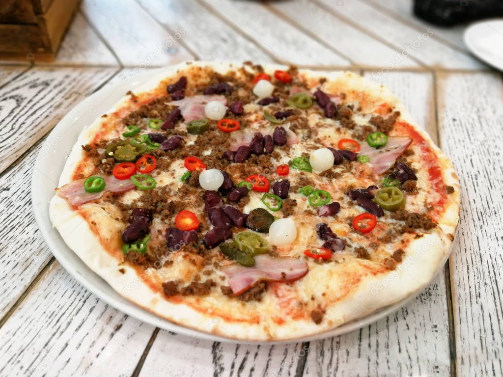 Spicy pizza with ham, mince, beans, chili pepper served on the aged wood table