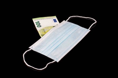 Tıbbi maskenin arkasındaki 100 Euro banknot siyah yansıtıcı arka planda izole edilmiş.