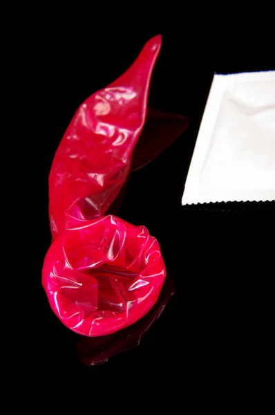 在黑色反光背景上隔离的性活动后使用粉红安全套 — 图库照片