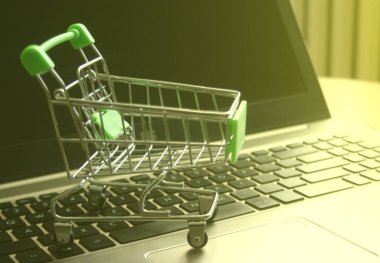 İş konsepti olarak pazarlama ve alışverişi simgeleyen dizüstü bilgisayar klavyesindeki mini alışveriş arabası.