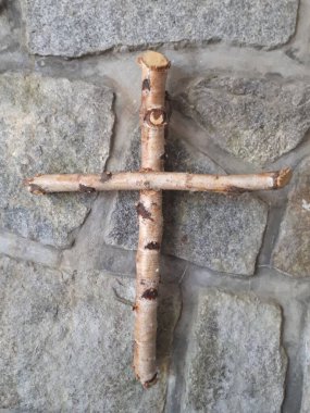 Wooden cross made of wooden sticks and birch branches on a background of stones clipart