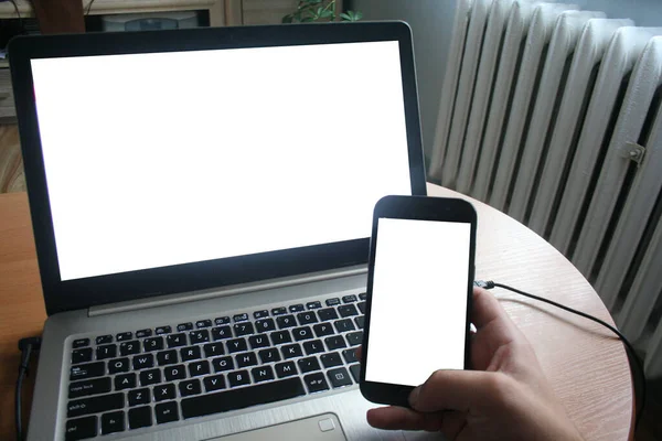 Close up of man using blank cell phone and laptop sending massages shopping online. The man works at the computer and receives the business phone.