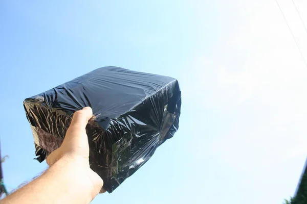 The package in a black box is held in the hand against the sky