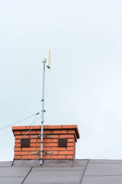 Ayrılmış bir evin kiremit çatısındaki bacaya sabitlenmiş bir internet anteninin düşük açılı görüntüsü