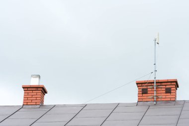 Ayrılmış bir evin kiremit çatısındaki bacaya sabitlenmiş bir internet anteninin düşük açılı görüntüsü