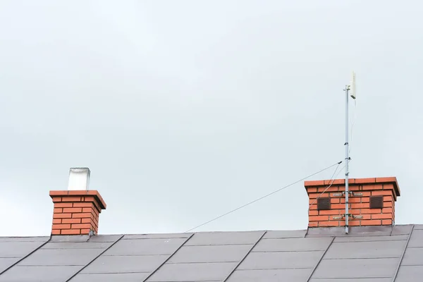 独立した家のタイル屋根の煙突に固定されたインターネットアンテナの低角度ビュー — ストック写真