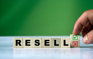 El, tahta küpü döndürür ve yeşil pozitif tik kutusu ve kırmızı reddetme X işaretli kutusuyla RESELL kelimesini değiştirir.