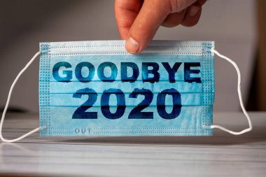 El, üzerinde GOODBYE 2020 yazan bir tıbbi ve koruyucu maske tutuyor. Koronavirüs karantinası kavramı. COVID-19 'un dünya çapında yayılmasını engelle ya da durdur.