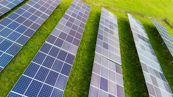 Günümüz tarım alanında yenilenebilir enerji teknolojisi sergilenen yemyeşil çimenler üzerinde sıralı olarak dizilmiş güneş panellerinin hava görüntüsü.