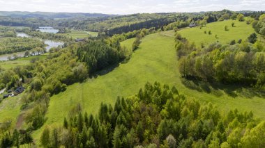 Vadide kıvrılan bir nehir ile yemyeşil tepelerin ve ormanların havadan görünüşü. Manzara, gün ışığında canlı bahar yaprakları ve huzurlu kırsal bölgeleri gösteriyor..