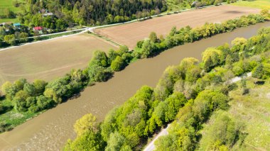 Baharda yemyeşil yemyeşil ve geniş tarım alanlarıyla çevrili sakin bir nehrin havadan görünüşü. Zengin renkler manzaranın doğal güzelliğini vurgular..