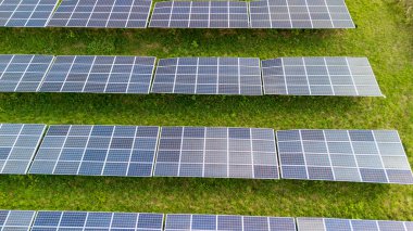 Yenilenebilir enerji üretiminde sürdürülebilir enerji çözümleri ve modern teknolojiyi temsil eden yeşil bir alan üzerine dizilmiş güneş panellerinin hava görüntüsü.