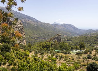 Guadalest İspanya 'daki dağlık manzaranın güzel panoramik manzarası yemyeşil kayalık uçurumlar ve öğle güneşinin altında açık mavi bir gökyüzü.