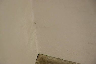 Açık renkli bir duvarda ince bir dokusu olan bir köşenin yakın görüntüsü. Tahta süpürgelik sahneye bir sıcaklık ve kontrast unsuru ekler..