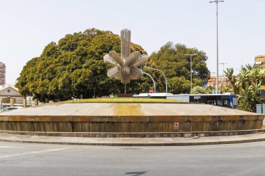 Alicante İspanya - 13 Temmuz 2025: Yeşillik ve kentsel mimariyle çevrili modern bir çeşme heykeli Alicante 'nin canlı kültürünü gözler önüne seriyor.