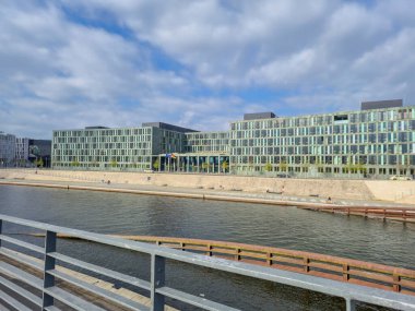 Berlin Almanya - 9 Nisan 2025: Rıhtım boyunca yer alan modern mimari, geniş cam pencereli ve manzaralı, sakin bir atmosferi olan çağdaş bir bina sergiliyor.