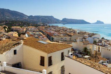 Altea İspanya - 17 Temmuz 2025: Altea 'nın panoramik manzarası terakotta çatıları ve turkuaz kıyı şeridi açık mavi gökyüzü altında büyüleyici beyaz binalar sergiliyor.