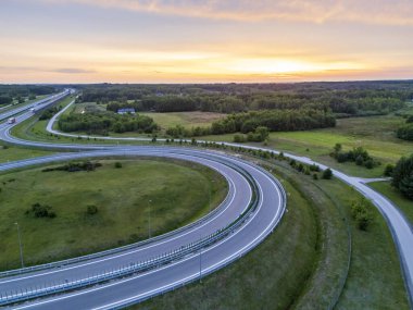 Gün batımında yemyeşil yemyeşil bir otobanın hava manzarası ufka giden yolun karmaşık kıvrımlarını gösteriyor..