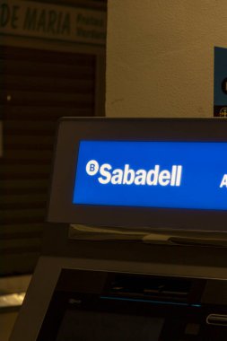 Alicante İspanya - 17 Temmuz 2025: Sabadell ATM arayüzüne yakın çekim geceleri bankacılık seçeneklerini gösteriyor. Aydınlatılmış tabela finansal hizmetlerin ulaşılabilirliğini gösteriyor.