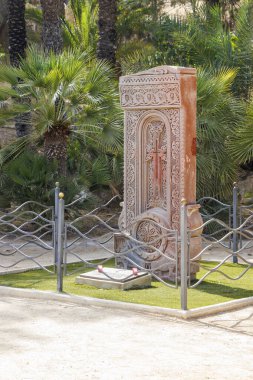 Alicante İspanya - 13 Temmuz 2025: Kültür mirası ve sanatsal işçiliğin sergilendiği huzurlu bir parkta bereketli palmiye ağaçlarıyla çevrili karmaşık şekilde oyulmuş taş bir anıt.