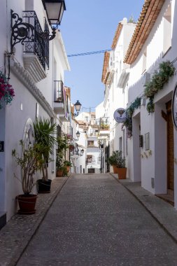 Altea İspanya - 17 Temmuz 2025: Beyazlatılmış binalarla dolu güzel dar bir cadde bitki saksısı ve dekoratif balkonlar Akdeniz köyünün cazibesini sergiliyor.