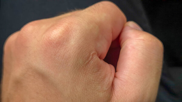 Close-up of a clenched fist symbolizing strength and determination. The hand is well-defined with skin textures visible showcasing emotions of grit in a neutral setting.