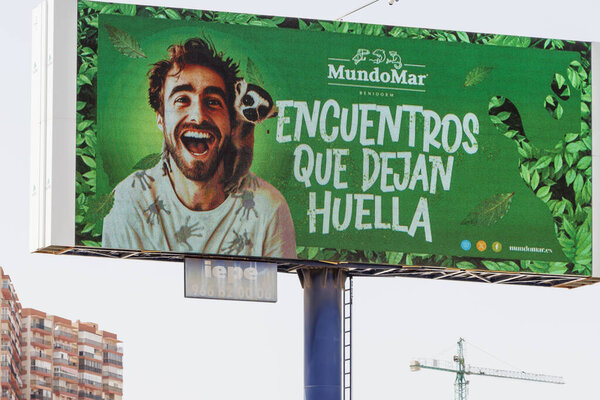 Аликанте Испания - 14 июля 2025: Яркий рекламный щит MundoMar показывает улыбающегося человека с обезьяной, продвигающей встречи дикой природы среди пышного зеленого дизайна.