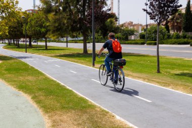 Alicante Spain - 14 Temmuz 2025: Genç bir adam, yeşil ağaçların oluşturduğu manzaralı bir patika boyunca bisiklet sürüyor ve sakin bir açık hava ortamı yaratıyor.