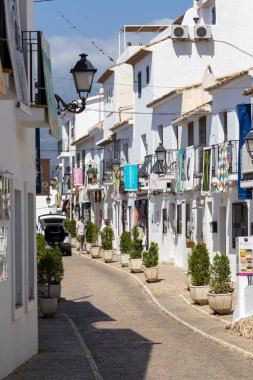 Altea Spain - 17 Temmuz 2025: Beyaz Akdeniz tarzı binalar ve renkli pankartlar ve saksı bitkileriyle dolu büyüleyici bir cadde ziyaretçiler için canlı bir atmosfer yaratıyor.