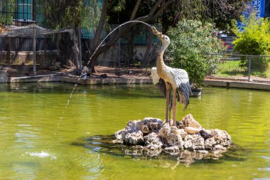 Alicante İspanya - 13 Temmuz 2025: Çevresi yeşil suyla çevrili küçük bir adada doğa ve sanat entegrasyonu sergilenen dekoratif bir vinç heykeli.