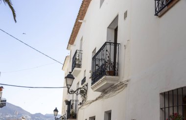 Altea Spain - 17 Temmuz 2025: Süslü balkonları olan büyüleyici beyaz binalar, bölgenin mimari güzelliğini ve Akdeniz yaşam tarzını gözler önüne seren güneşli bir cadde..