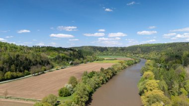 Güneşli bir günde yemyeşil tarlalarda ve ormanlarda dolaşan sakin bir nehrin havadan görünüşü. Doğa ve manzara fotoğrafçılığı için ideal..
