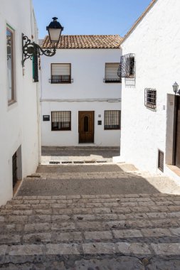 Altea İspanya - 17 Temmuz 2025: Altea 'da güneşli bir caddenin manzarası kaldırım taşı basamaklarından inen demirden yapılmış geleneksel beyaz binalar sergileniyor.