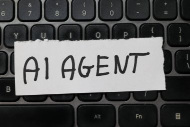 Bilgisayar klavyesine yerleştirilmiş yırtık bir kağıt parçasına el yazısıyla yazılmış yapay zekanın modern teknoloji ve iletişimdeki rolünü belirtir..