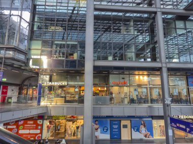 Berlin Almanya - 9 Nisan 2025: Berlin Hauptbahnhof 'da Starbucks ve Essenziale' in yer aldığı modern mimari ve canlı atmosfer içeren dükkan ve kafelerin manzarası.