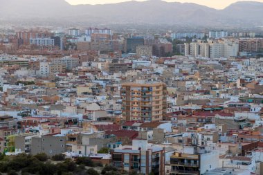 Günbatımında çeşitli binalarla dolu yoğun bir şehir manzarasına sahip Alicante şehri geziler ve emlak temaları için mükemmel mimari ve dağ zeminini sergiliyor..