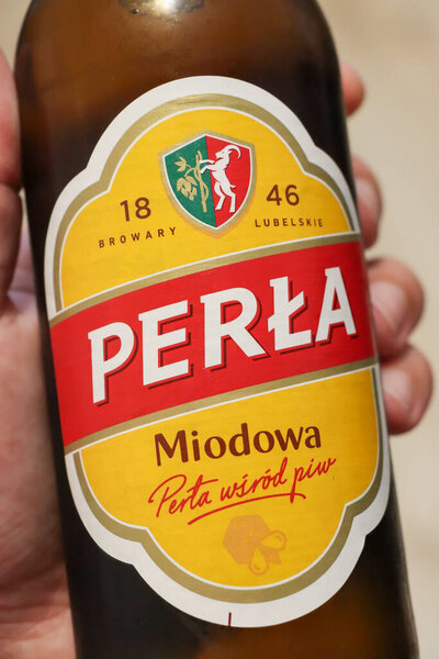 Warsaw Poland - August 2 2025: Close-up of a hand holding a bottle of Perla Miodowa beer showcasing its distinctive label and branding.