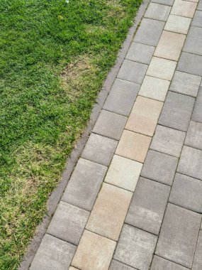 Taze yeşil çimenlerin bitişiğindeki desenli taş patikanın yakın görüntüsü zıt dokuları ve renkleri gösteriyor. Peyzaj ve açık hava tasarımı için ideal..