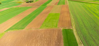 Yeşil ve kahverengi bölgelerin karışımından oluşan canlı tarım alanlarının havadan görünüşü. Planda kırsal alanda modern tarım teknikleri sergileniyor..