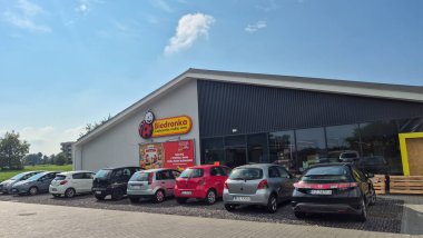 Rzeszow Polonya - 9 Eylül 2025: Açık mavi gökyüzünün altında park halindeki arabaların bulunduğu Biedronka mağazasının manzarası canlı bir market alışveriş atmosferi sergiliyor.