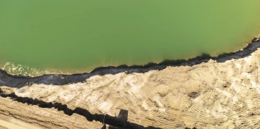 Yeşil su gövdesine sahip kumlu bir sahilin havadan görünüşü tortul doku ve doğal manzara sergiliyor. Doğa ve çevre çalışmaları temaları için ideal.