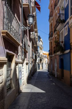 Alicante Spain - July 17 2025: A narrow cobblestone street lined with colorful buildings featuring classic architecture bathed in bright sunlight offering a charming urban atmosphere.