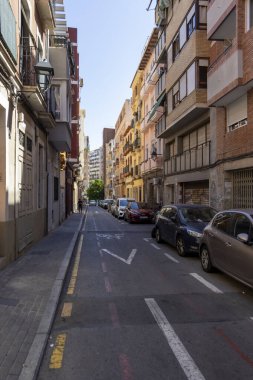 Alicante Spain - July 17 2025: A quiet urban street scene showcasing colorful residential buildings parked cars and clear blue sky illustrating typical city life.