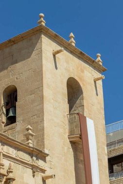 Alicante Spain - July 17 2025: Clear view of a historical buildings tower featuring a bell and intricate architectural details against a blue sky.